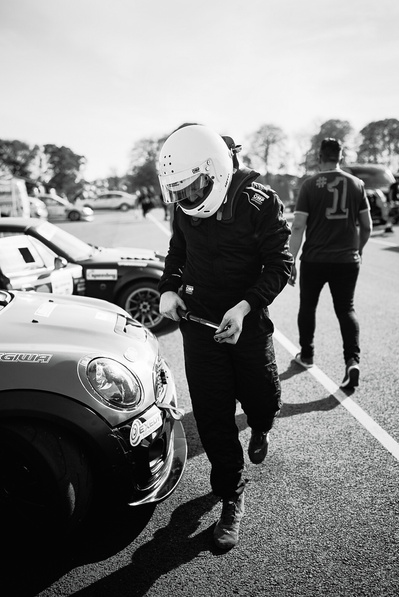Time Attack UK car racer with white helmet on and ratchet in his hand wearing race overalls ready to tighten wheel nuts before competing with his MINI R56 race car. 