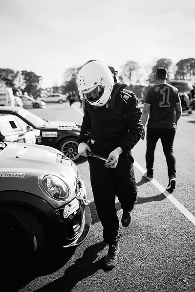 Time Attack UK car racer with white helmet on and ratchet in his hand wearing race overalls ready to tighten wheel nuts before competing with his MINI R56 race car. 