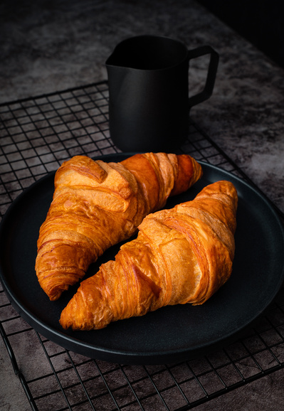 dark food photography shot in a studio of two golden Croissants on a black plate with dark background and on a concrete texture surface.