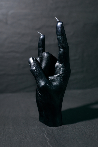 a black wax candle of a hand photographed in a studio on black slate.
