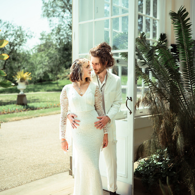 Alternative couple having wedding photos taken in the door way of a botanical gardens in Sheffield with cacti in the foreground. She wears a white alternative boho goth dress and he has a white suit.