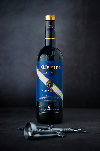 a bottle of red wine and a bottle opener in a studio with a dark backdrop.  Product photography by Rob Senior