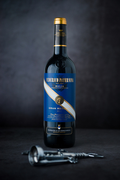 a bottle of red wine and a bottle opener in a studio with a dark backdrop.  Product photography by Rob Senior