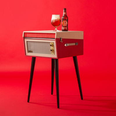 vintage record player with a bottle of beer and a glass of beet on top in a studio with a red seamless background.