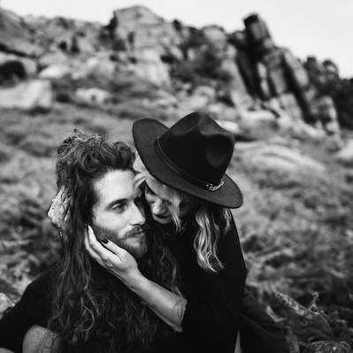 Newly engaged couple having an engagement photo shoot at the roaches in the peak district. Alternative couple wearing black with tattoos and piercings looking at each other in love.