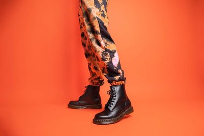 Black Dr Martens boots photograph taken in a studio on a female model wearing orange trousers on an orange seamless backdrop