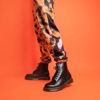 Dr Martens boots in Black shot in a photo studio with a model wearing orange trousers on an orange backdrop