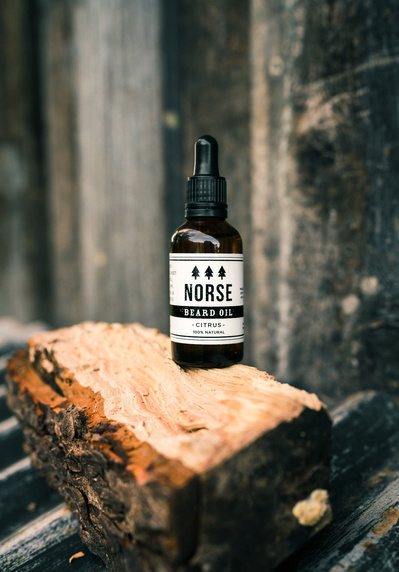 a product shot of a bottle of Norse Beard Oil photographed on a log in a rustic setting.
