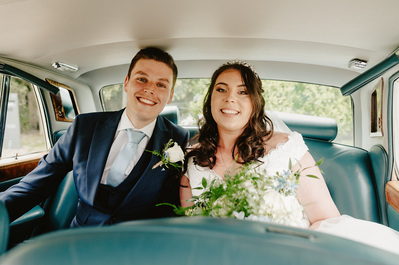 Photograph of bride and groom, smiling in the back of a wedding car at Chapel house estate