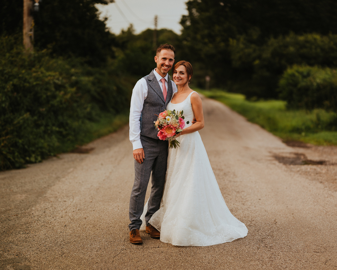 relaxed wedding photography portrait of a newly married couple standing in the middle of a road in the middle of the kent countryside looking at the camera
