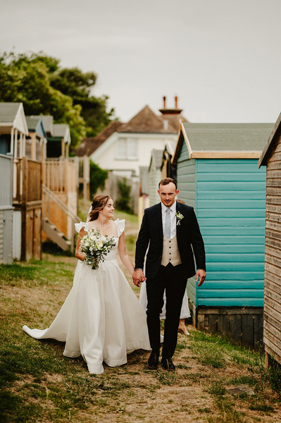Bride and groom walking along the coast with Beacon house in the background