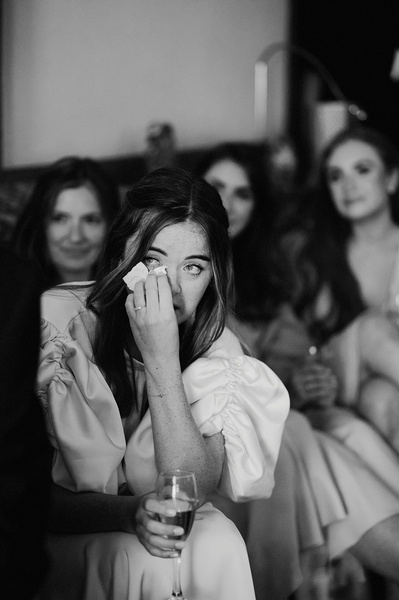 Black and white photo of Bride wiping away emotional tears from her eyes during her father's speech