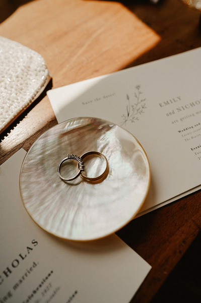 Wedding rings are sitting on top of wedding invite in natural light by window
