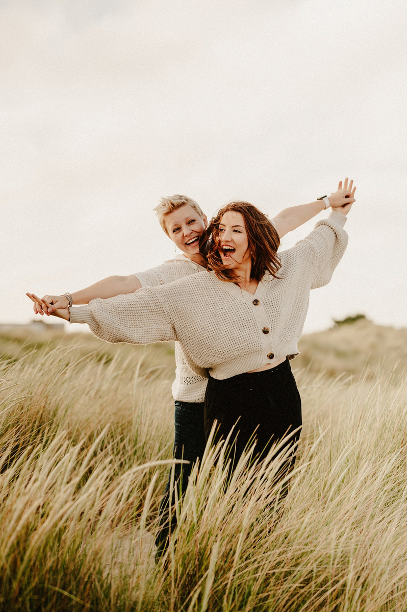 engagement photography on a kent beach standing in long grass holding hands up high whilst pretending to fly