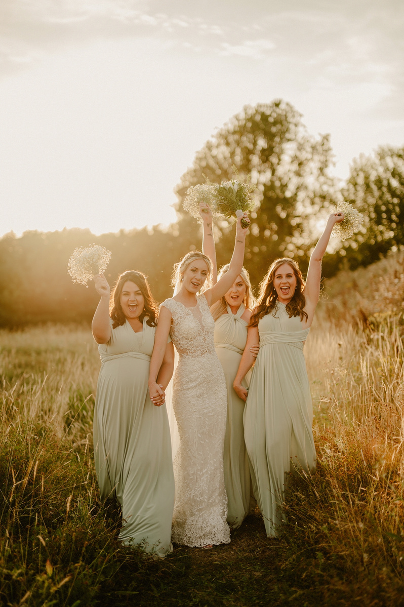 relaxed bridesmaids during golden hour holding their flowers up above their heads whilst walking towards kent wedding photographer and laughing trying not to fall over