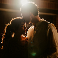 relaxed low-light wedding photography portrait at a shallow depth of field after a garden wedding reception in kent, the couple are only lit by a garage flood light creating a beautiful lens flare whilst the groom kisses the bride on the forehead