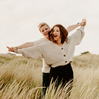 engagement photography on a kent beach standing in long grass holding hands up high whilst pretending to fly
