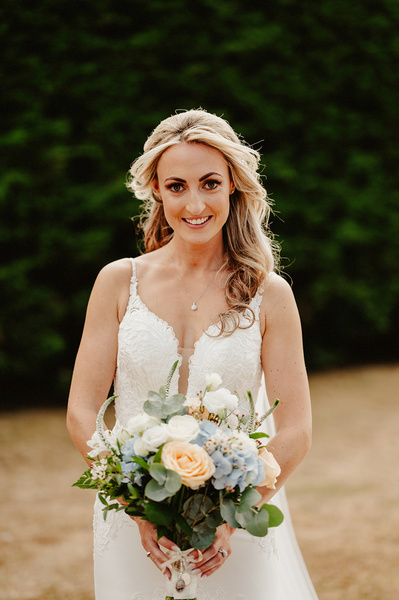 stunning portrait of bride in white wedding dress in front of hedge smiling at the camera at winters barns