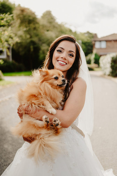 Bride smiling whilst holding her dog on a street in Kent