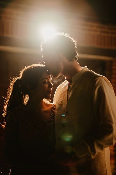 A wedding portrait of bride and groom wearing traditional clothes with a flare from a bright light behind them
