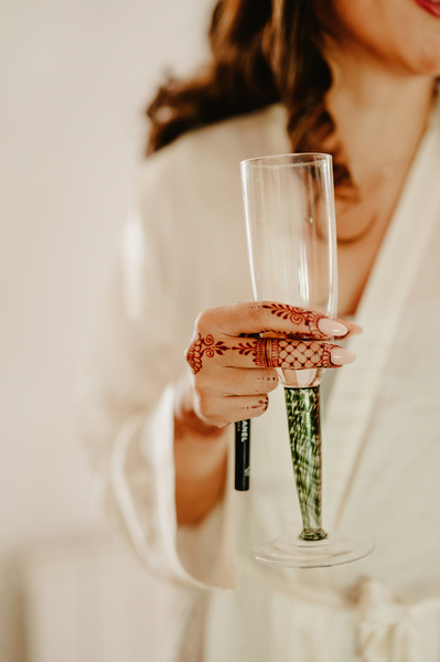 A champagne glass being held by a bride with a henna on her fingers