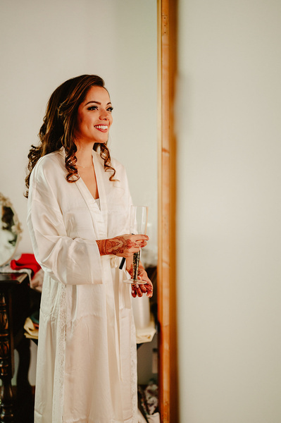 Candid photograph of a bride with henna on her hands are holding a glass of champagne on her wedding day