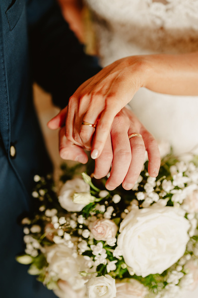 Bride and groom hold hands showcasing their wedding rings on top of flowers at Marleybrook House