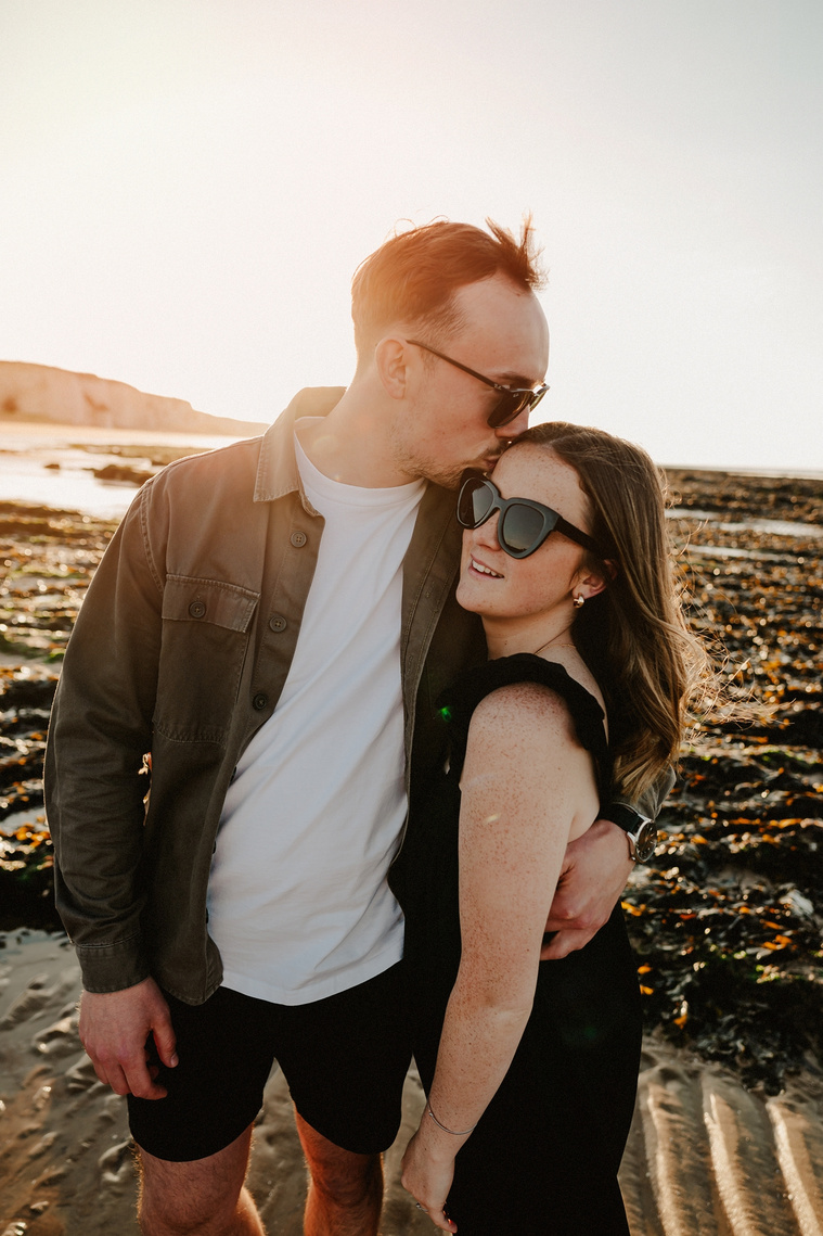 Man kisses his bride to be on the forehead during sunset at botany Bay Kent