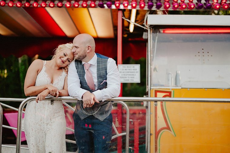 newly weds pose for a photo and cuddle into each other in front of an antique rollercoaster at marleybrook house