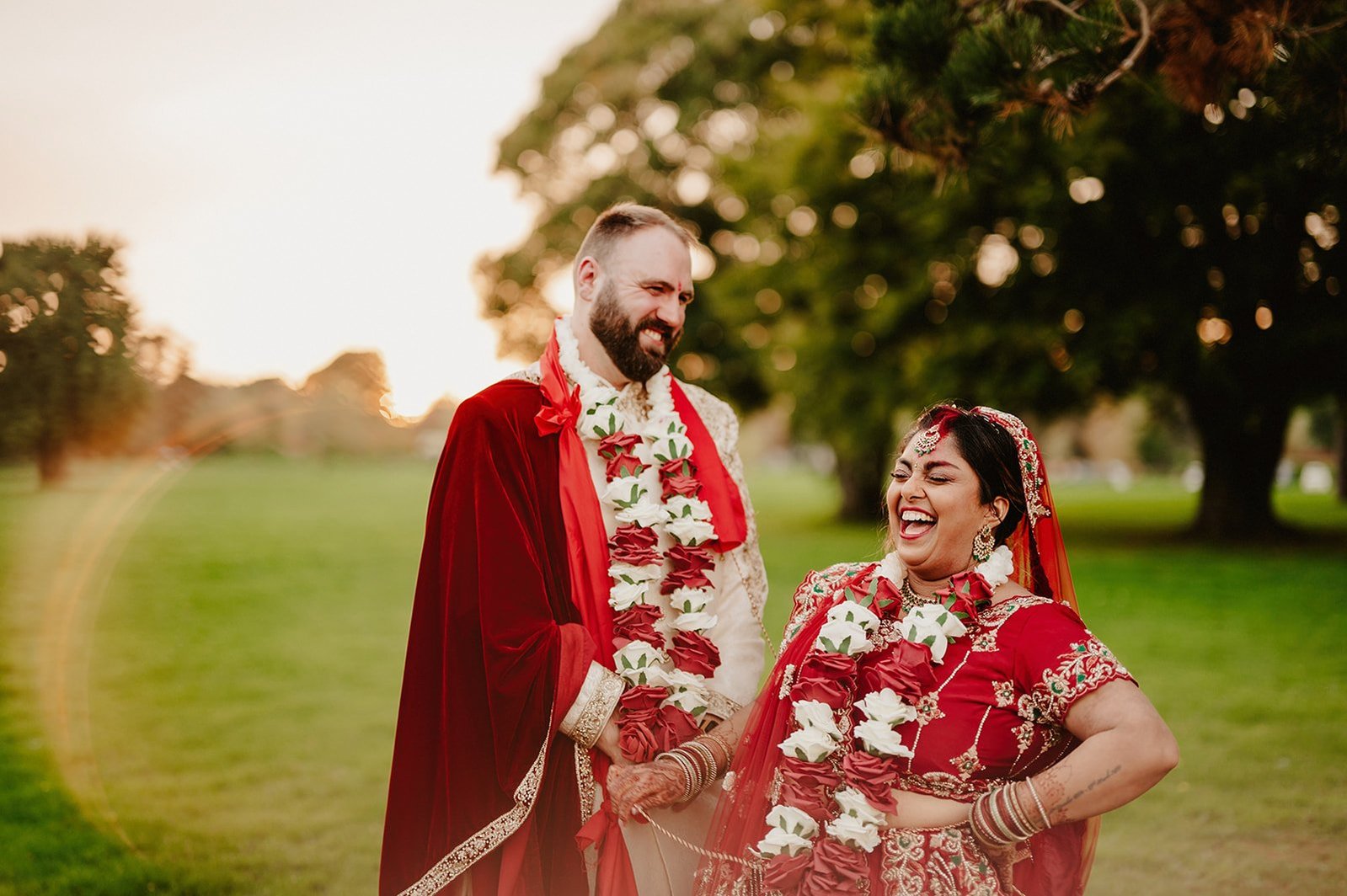married couple in traditional indian wedding outfits laugh and enjoy the sunset at hayne house in kent