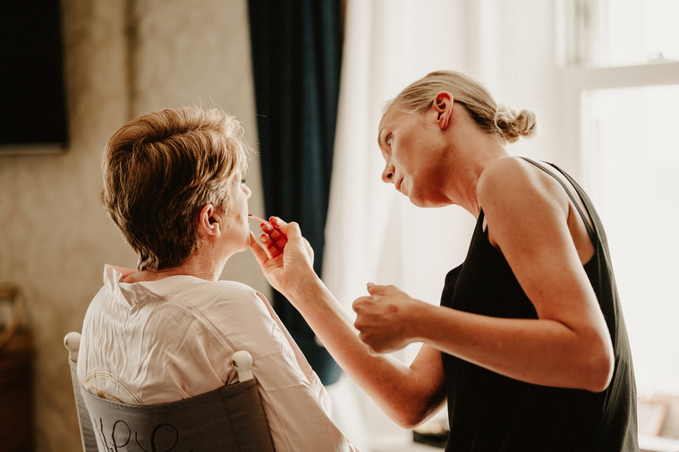 A serene moment as a makeup artist gently applies the mother of the bride's makeup before the ceremony, capturing the relaxed atmosphere of the wedding day