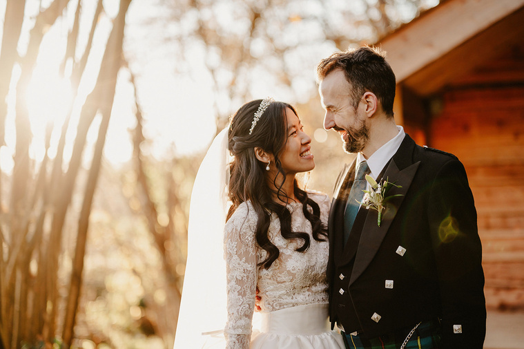 A radiant and relaxed portrait of a bride and groom during the golden hour, sharing warm smiles, beautifully enhanced by a captivating lens flare