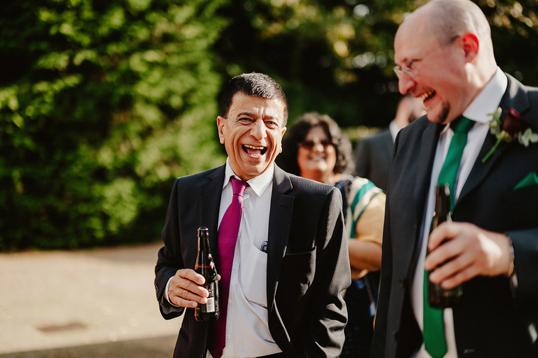 A cheerful wedding guest savoring a refreshing drink during the relaxed outdoor drinks reception, embodying the joyous atmosphere of the celebration