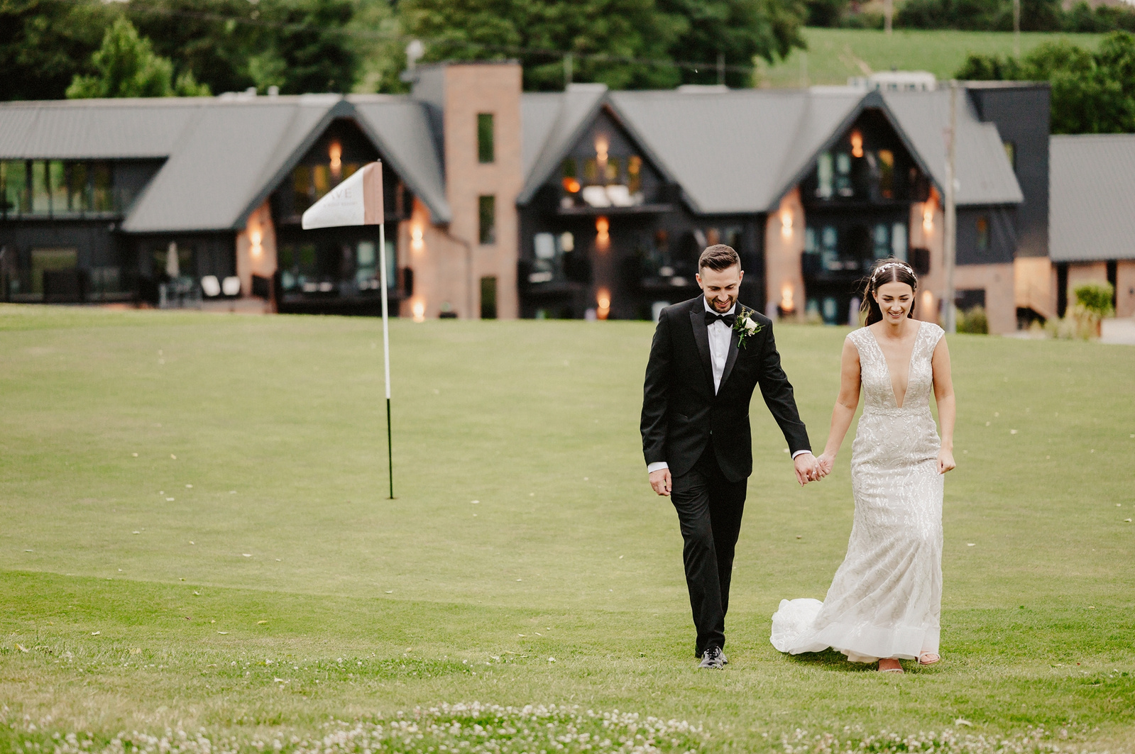 Bride in a wedding dress walks with her tuxedo wearing groom on the golf course with cave hotel kent behind them