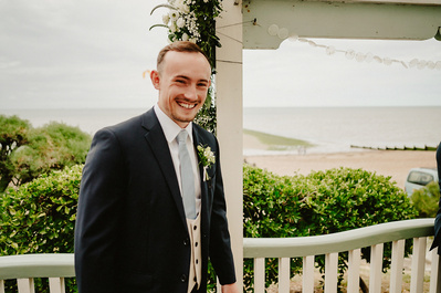 Groom smiling at the camera with the sea behind him