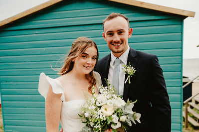 Bride and groom in Whitstable standing in front of a beach huts for a Portrait