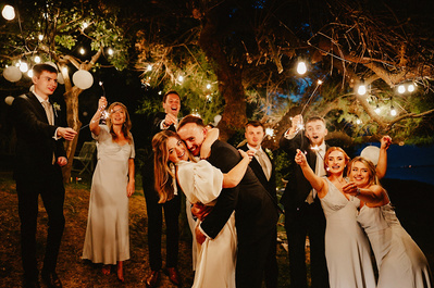 Everyone holding sparklers under a lightbulb tree all smiling and laughing
