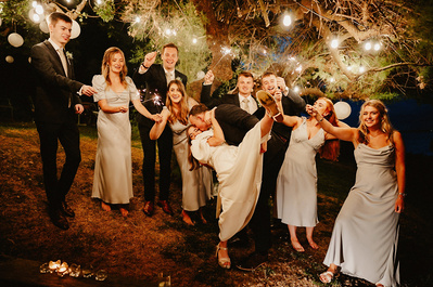 Bride and groom surrounded by their bridal party under a low lit tree holding sparklers