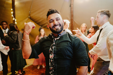 Male wedding guest at kent Indian wedding smiling for the camera whilst tensing his biceps
