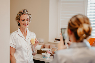 Bridesmaid takes a photo with her phone of the bride while she smiles happily in the salon at winters Barns
