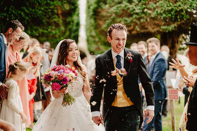Bride and groom laughing and joking whilst being showered with confetti outside a Kent church
