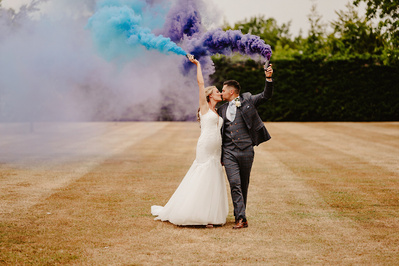 bride and groom portrait of them kissing whilst holding colourful smoke grenades