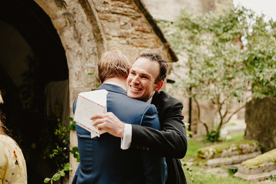 Candid photo of a groom hugging a wedding guest outside a church