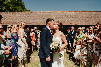 An outdoor first kiss with the wedding guests in the background of the photo