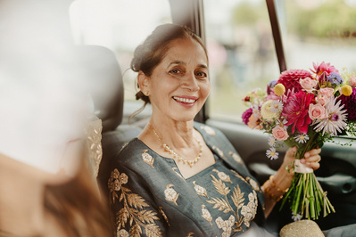 Photo shot through a car window of the mother of the bride smiling I was holding flowers before the wedding ceremony in a Kent Church