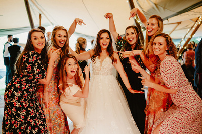 Wedding guests on the dancefloor surround the bride smiling and pointing