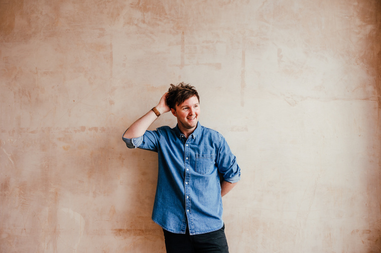 Kent wedding photographer James is posing in front of a distressed wall smiling for a Portrait wearing a denim shirt