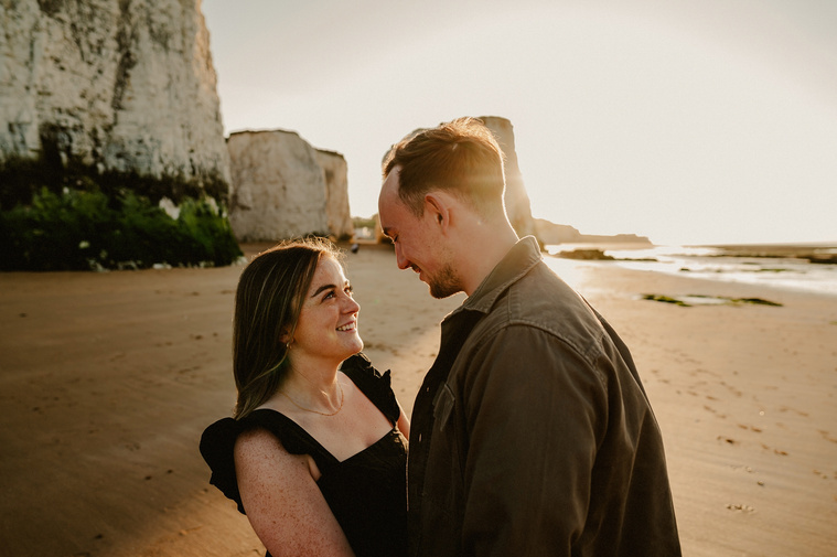 woman smiles lovingly at her fiance on botany bay during golden hour