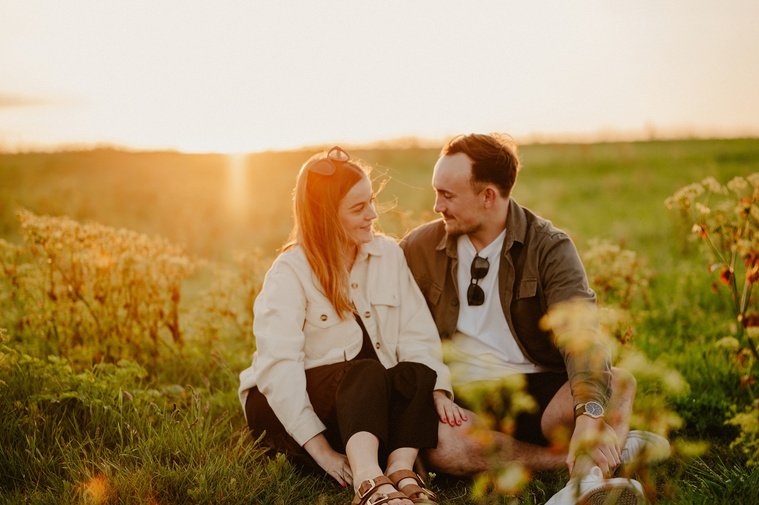 Happy couple nestle into each other during golden hour on the grassy cliff tops at the botany bay beach in kent