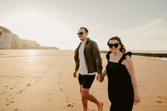 Future bride and groom laughing running towards the camera on botany bay beach with the sea in the background